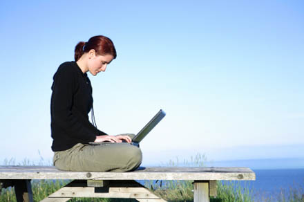 Young woman working on a laptop on a rustic environment outdoors.